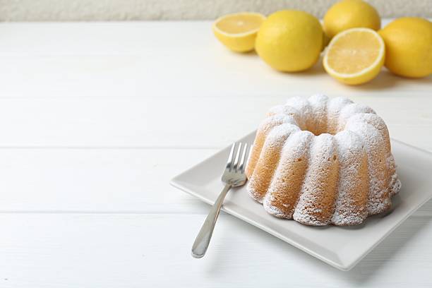 Delicious lemon cake with powdered sugar and fork on white wooden table, closeup. Space for text