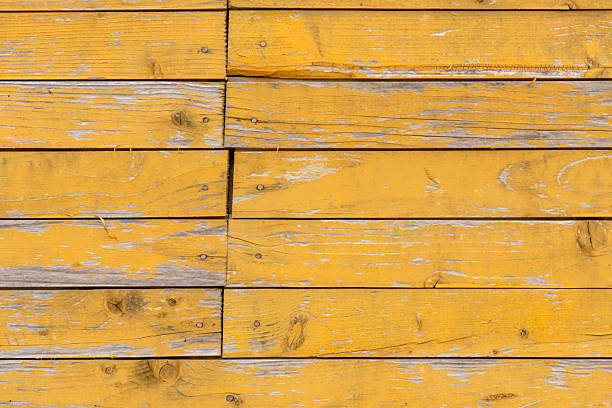 Rustic wood surface composed of horizontal planks painted in faded yellow, with peeling layers revealing natural grain, knots, and imperfections. A single round hole adds character to the aged texture. Ideal for vintage design, architectural backgrounds, or distressed material references in digital art and modeling.