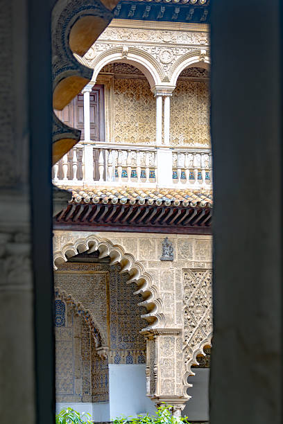 View through a narrow opening revealing detailed Moorish arches, carved stone columns and decorative tiles in a historic Andalusian courtyard