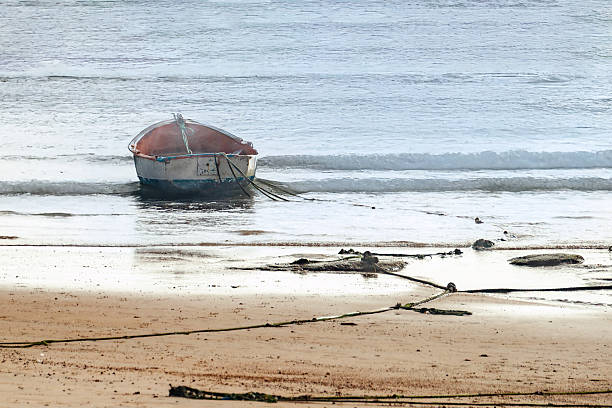 Small weathered boat tethered by ropes near the water’s edge, resting between wet sand and gentle waves