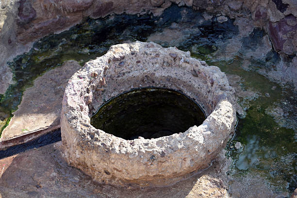 A detailed view of an old stone well highlights erosion, mineral buildup, and organic wear from long-term use. The circular opening draws the eye into the structure, symbolizing depth, resources, and survival. Ideal for storytelling around history, archaeology, water access, and traditional construction methods.