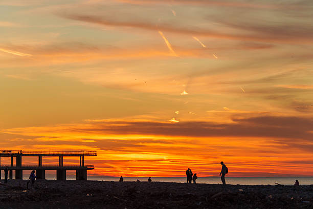 Sunset Beach Scene with Pier and Silhouetted People Under Vibrant Orange Sky. High quality photo