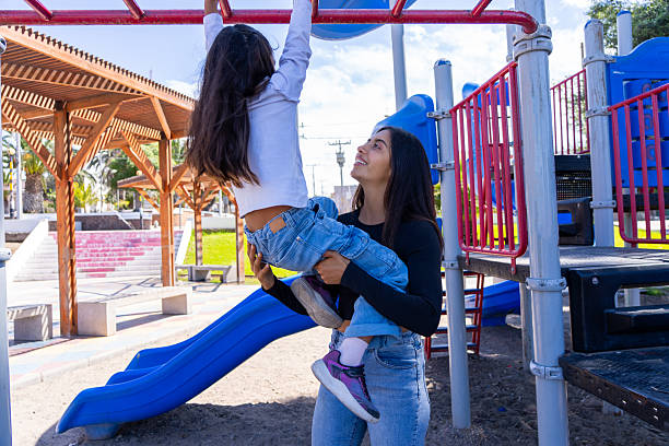 istock Mother lifting daughter, assisting her on the monkey bars in a park 2255106400