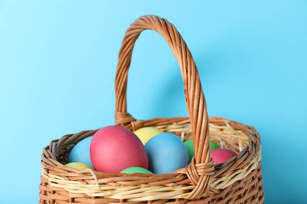 Beautiful decorated Easter eggs in wicker basket on light blue background, closeup