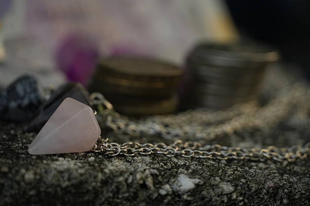 A delicate rose quartz pendant, attached to a fine silver chain, is the central focus of this image, captured with a soft depth of field. In the gently blurred background, hints of coins and a 20 pound banknote are visible, contrasting material and spiritual value.