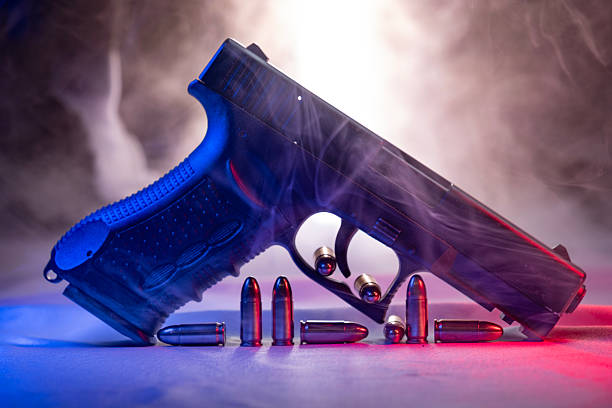 A black semi-automatic pistol is displayed alongside several loose cartridges on a surface, emphasizing themes of crime, danger, and conflict.