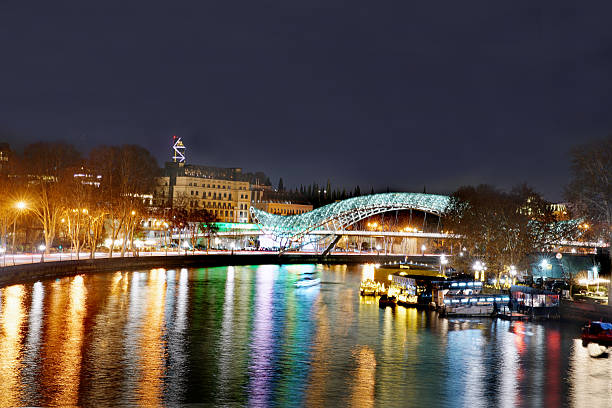 Night view on Pedestrian bridge and Kura river and some skyscraper  in distnce . Some yellow cafe on ship in river