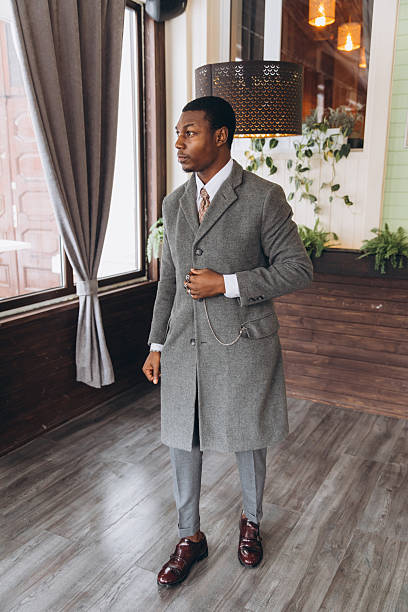 African American man in dapper overcoat and suit standing indoors, exuding elegance and classic style