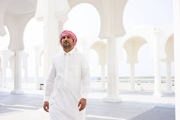 Middle eastern man walking in a modern white arched corridor, representing traditional culture and architecture in a bright, contemporary setting under daylight