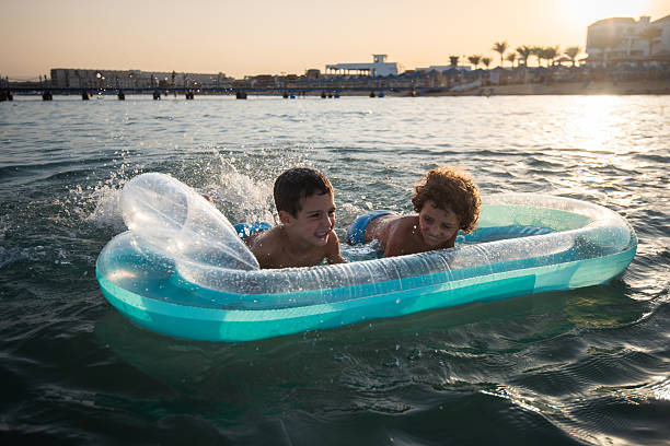 Children having fun on inflatable boat in ocean at sunset.