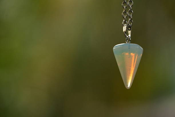 This serene image captures an opalite crystal pendulum suspended by a silver chain, with a soft, natural green background.