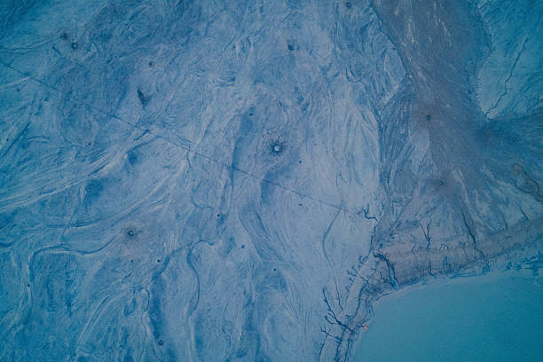 Mesmerizing aerial top view of a frozen lake surface featuring windblown snow and dark ice cracks. The high contrast abstract pattern creates a stunning winter background resembling marble stone or fluid art.