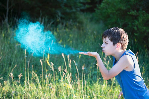 Boy blows bright blue color powder from his hand outdoor. Holi celebration, youth expression, festive rituals, creative motion, cultural traditions, and vibrant color play.