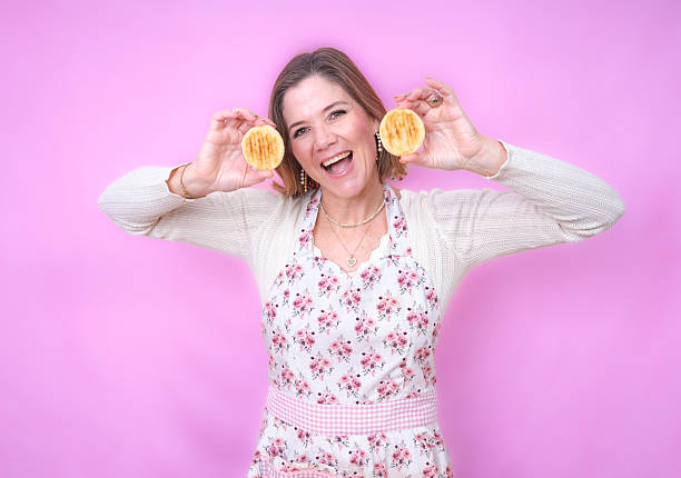 Woman in floral apron happily presenting two freshly cooked arepas with a smile