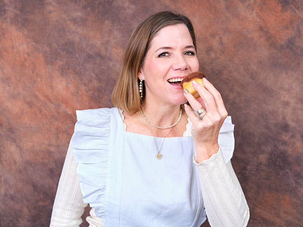 Woman smiling eating cupcake wearing blue apron