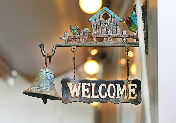 A rustic 'Welcome' sign featuring a charming birdhouse and a classic metal bell, hanging beautifully to greet visitors with a warm, vintage touch.