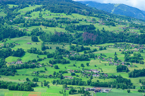 Scenic aerial view of lush green valley with houses and forested hills in summer landscape.