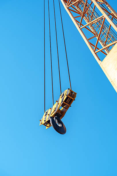 Industrial crane boom and hook against a sunny blue sky