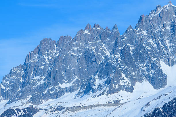 Rugged granite spires of Aiguille de Blaitiere rise dramatically above snowy alpine slopes under a vivid blue sky, showcasing sharp rock textures and winter contrasts.