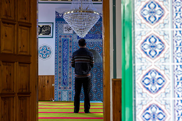 Man performing islamic prayer inside a mosque, kneeling on prayer rug with peaceful and spiritual atmosphere during worship