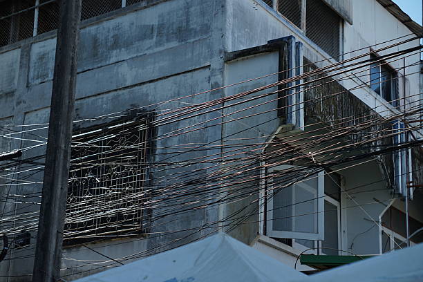 Footage showing a chaotic bundle of black electrical wires and internet cables hanging across the exterior wall of an old concrete commercial building (shophouse). The scene captures the disorganized urban infrastructure and gritty atmosphere typical of Southeast Asian cities.