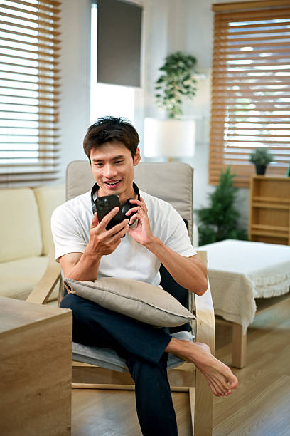 A man relaxes at home with headphones around his neck while using his mobile phone