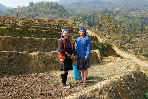 Two ethnic minority women in traditional attire standing on terraced hillsides in Northern Vietnam, showcasing local culture and agriculture.