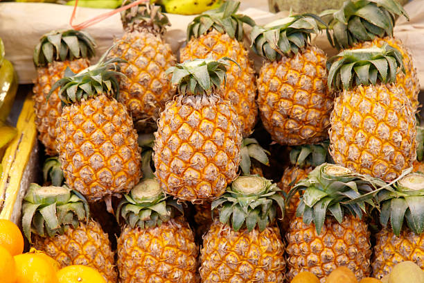 A pile of pineapples with a yellow top. There are many pineapples in the pile