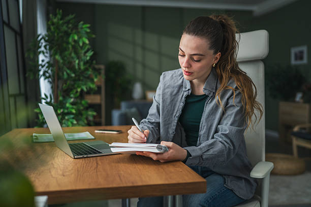 istock Young woman smiling writing in notebook during home office 2255182435
