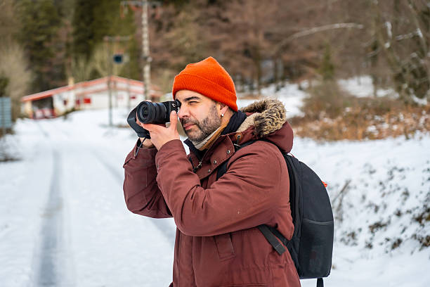 istock Man photographing winter landscape with camera and orange hat 2255185003