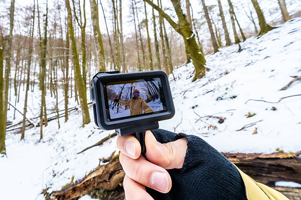 Person holding a compact action camera, recording a selfie video while hiking through a snow-covered forest, capturing a solo adventure in the tranquil winter outdoors