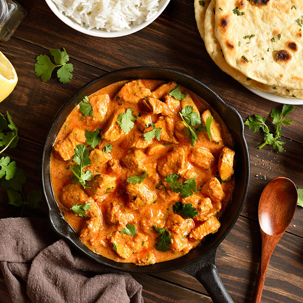 Chicken tikka masala curry in cast iron pan on wooden background