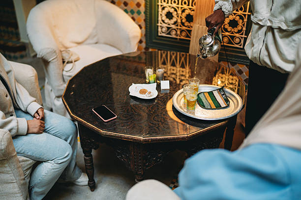 Person pouring warm Moroccan mint tea into small glasses for guests in a traditional riad setting. Hospitality concept