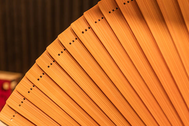 This macro shot captures the intricate detail of a traditional folding fan made from high-quality bamboo. The focus is on the overlapping ribs, which are fanned out to reveal a warm, orange-brown hue and a smooth, varnished natural grain. Small, precision-drilled holes line the edge, likely for the binding string or rivet that connects the slats. The rhythmic, stepped arrangement creates a satisfying geometric pattern, while the shallow depth of field softens the background, emphasizing the craftsmanship of the bamboo structure.