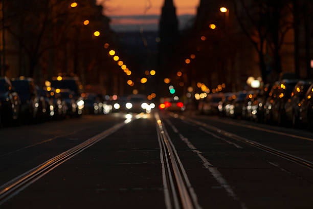 tram rails stretching toward glowing bokeh, moving headlights and parked cars create cinematic lane rhythm, pavement reflecting