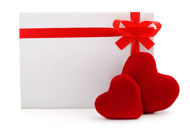 Blank white card decorated with a red satin ribbon bow and two plush hearts. Romantic template for Valentine Day, wedding or birthday isolated on white background. Love and celebration concept.