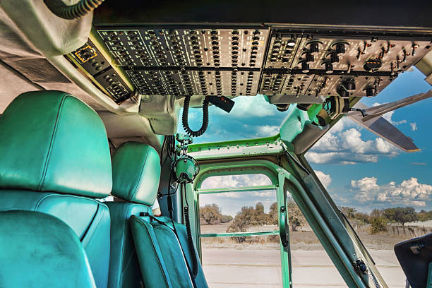 View from the passenger cabin into the cockpit of a vintage military helicopter, featuring green seats, overhead control panels, and an open door looking out over a rural landscape
