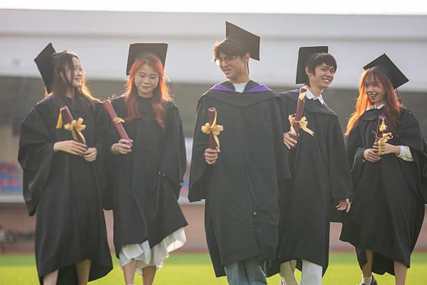 A group of young university students celebrate their success outdoors, proudly holding their diplomas to mark the completion of their studies.