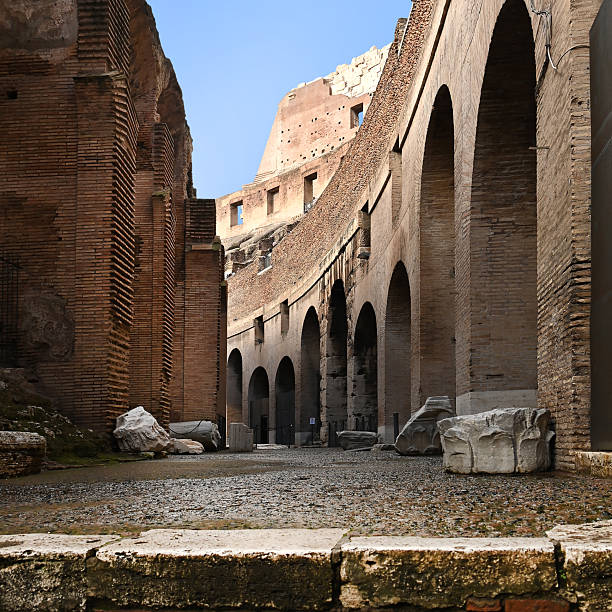 Interior of Rome colosseum amphitheatre with historic archway, sunlit brick walls, step and stone fragments, in square format