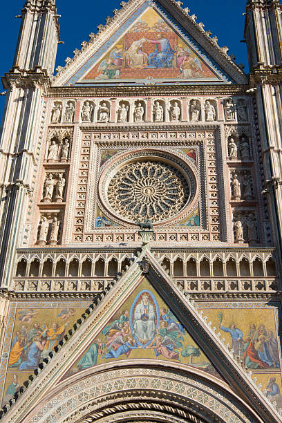 Details of Orvieto cathedral facade showcasing gothic architecture, mosaics, and bas-reliefs under a blue sky.
