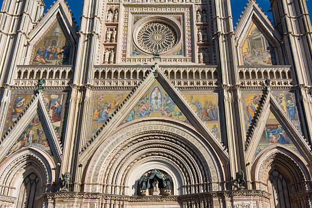 Details of Orvieto cathedral facade showcasing gothic architecture, mosaics, and bas-reliefs under a blue sky.