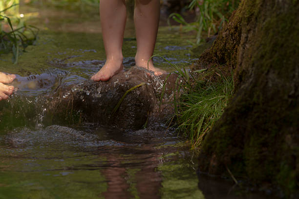 A person is standing barefoot on a rock in the flowing water of a watercourse, enjoying leisure time in natures beautiful surroundings