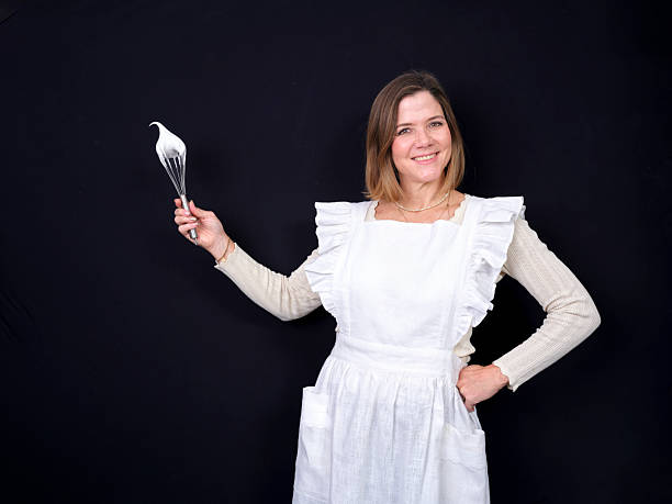 Woman smiling while holding a whisk with fluffy meringue peaks on a black background