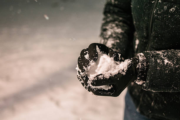 Person wearing black gloves holding fresh snow on a cold winter day. Winter season, cold temperature, outdoor lifestyle concept.