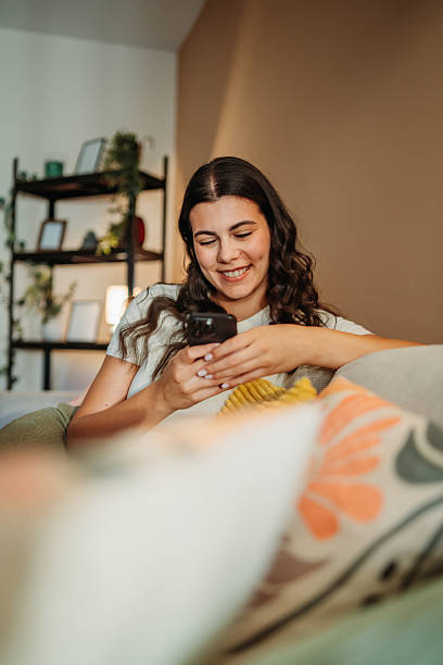 istock Young woman smiling using smartphone sitting on couch 2255210576