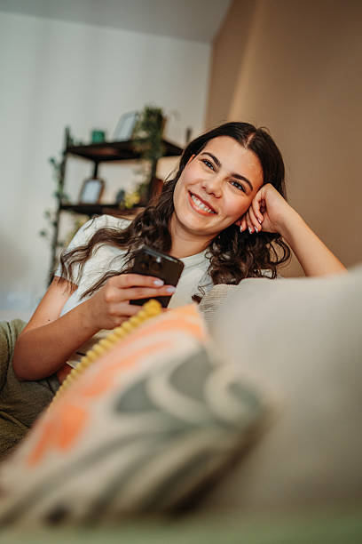istock Young woman smiling holding mobile phone relaxing on sofa 2255210580