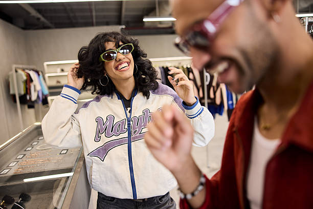 At a shop, a man and a woman try on sunglasses and look at each other.