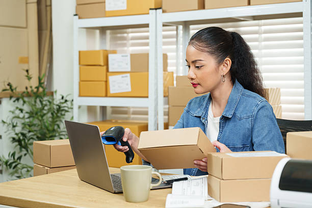 istock Asian woman small business owner checking parcel box shipping address using barcode scanner beside laptop packaging desk ecommerce order verification home warehouse online shop daily work 2255215454