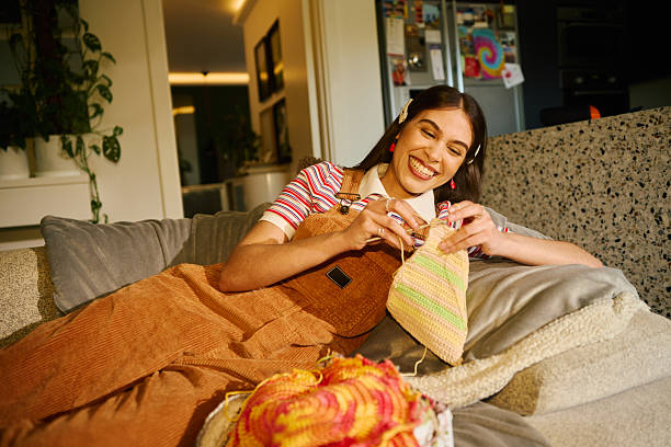 Young adult woman relaxing on sofa, crocheting colorful yarn, enjoying a creative hobby