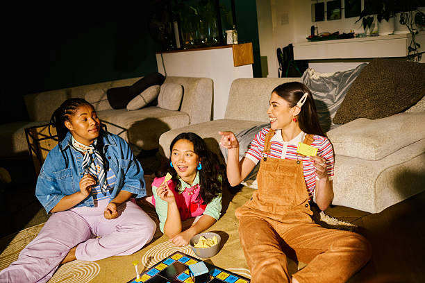 Group of diverse young adult women enjoying board game night, laughing, eating snacks and having fun